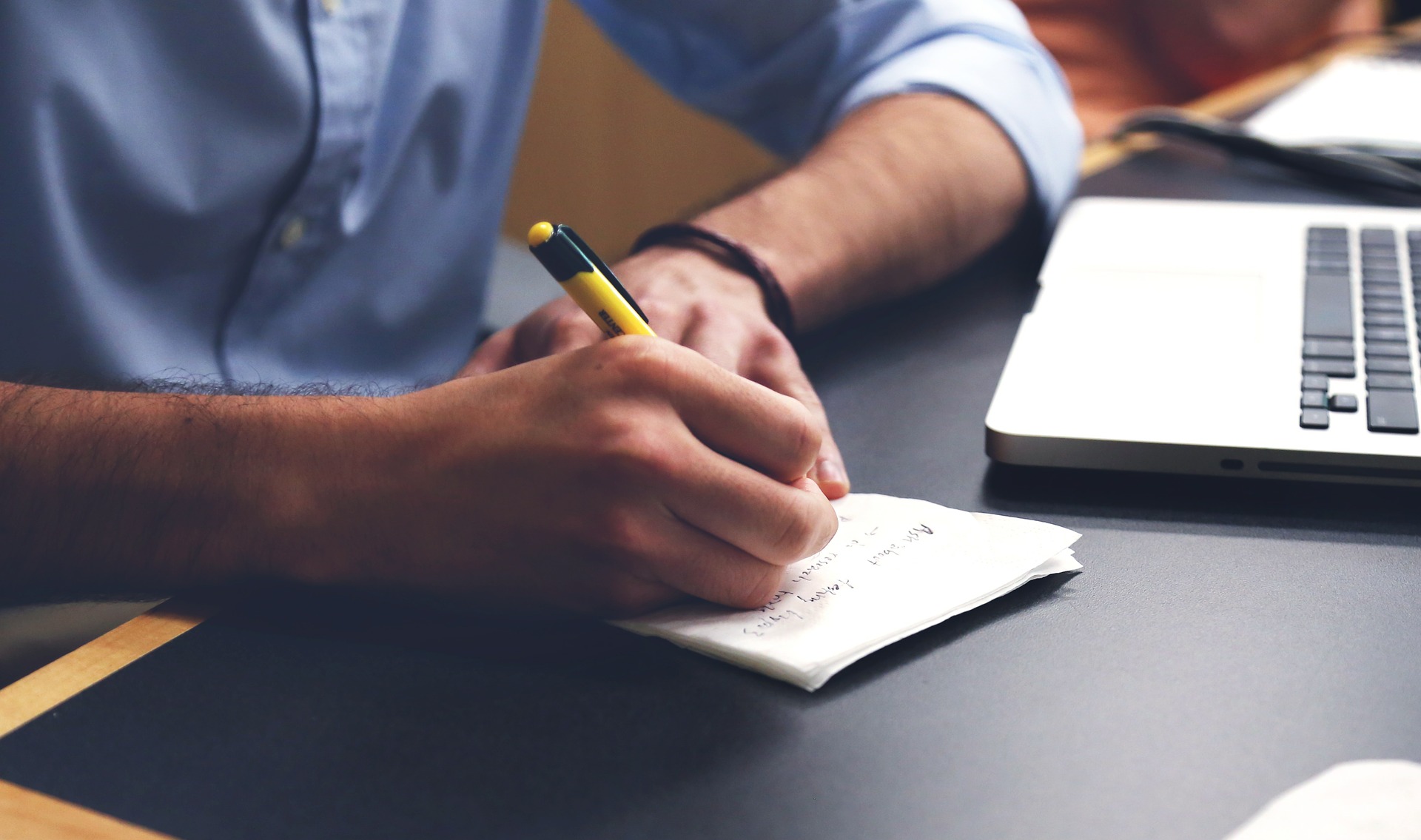 man writing on a paper in front of laptop