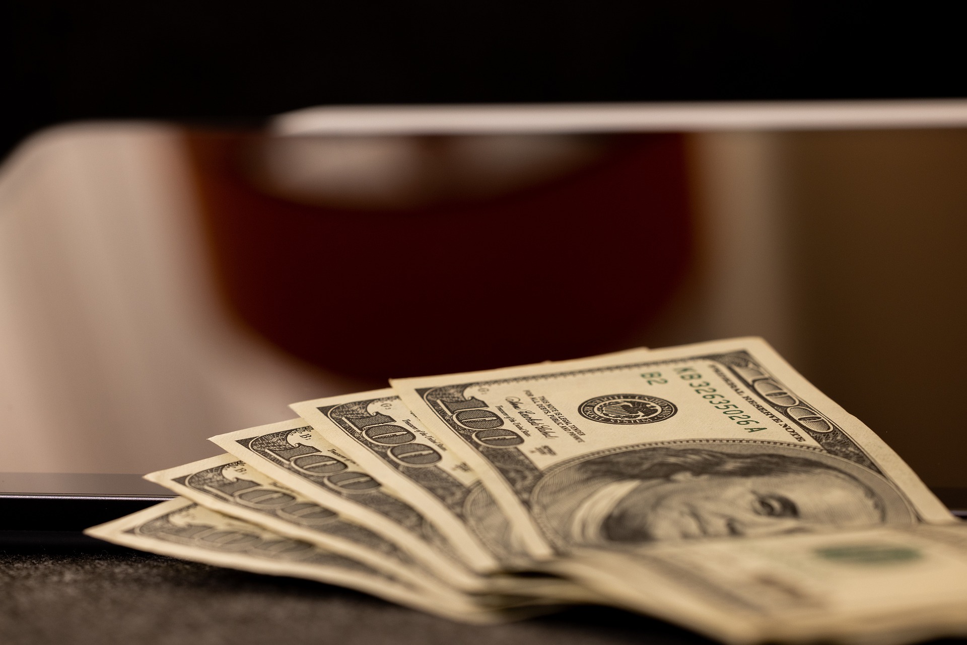 five one hundred dollar bills fanned out on dark surface